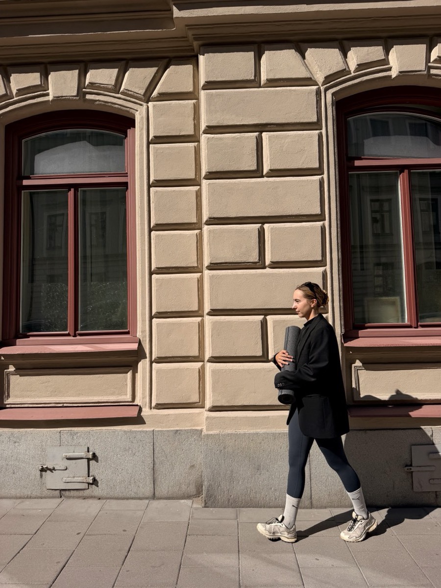 Camilla walking with a yoga mat past a sandstone facade in Stockholm